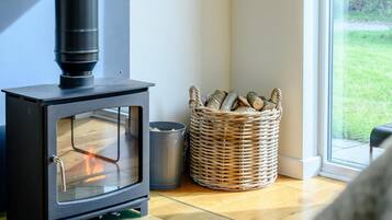 A room with a wood-burning stove, a wicker basket with logs, and a view of the outdoors through a window.