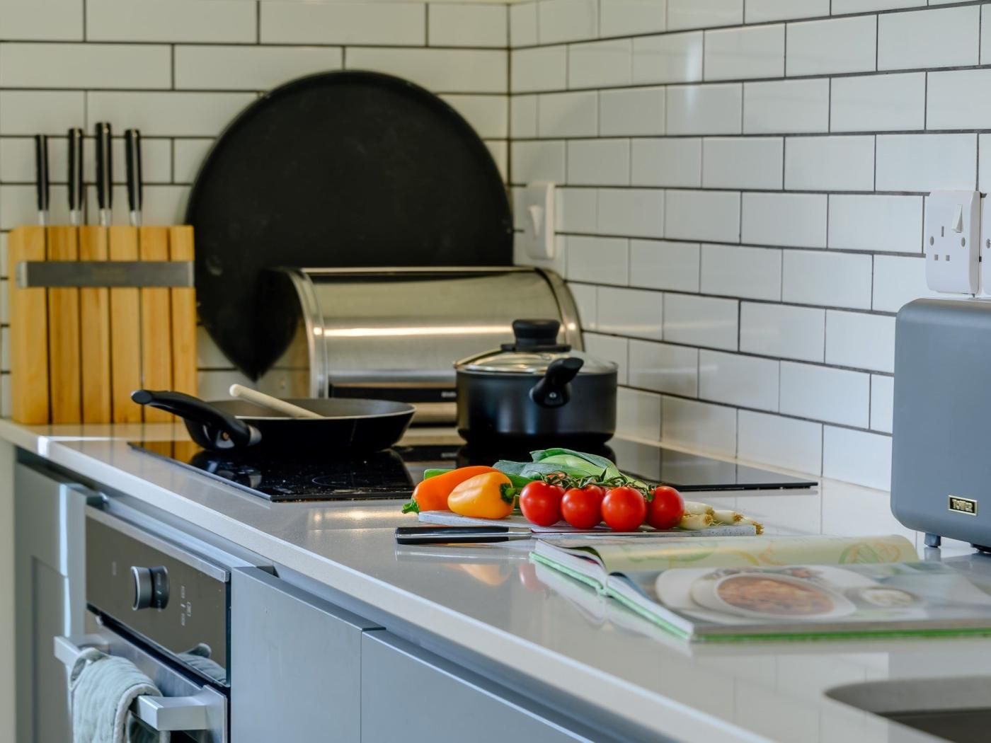 A kitchen with a stove, a frying pan, a pot, and some vegetables on the counter.