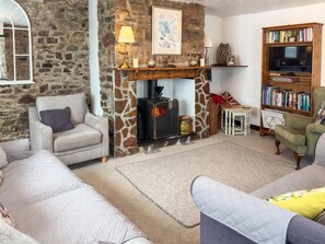 A cozy living room with a stone wall, a fireplace, a sofa, a bookshelf, and a television. - 3 Bed in Bideford (oc-88143) (Hartland)