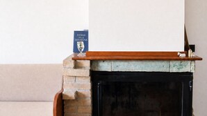 Ein Kamin mit Ziegelumrandung, einem hölzernen Sims und einem Buch mit dem Titel 'Storia di Sardegna' darauf.