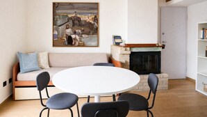 Ein Wohnzimmer mit einer Couch, einem runden Tisch, Stühlen, einem Kamin und einem Bild an der Wand.