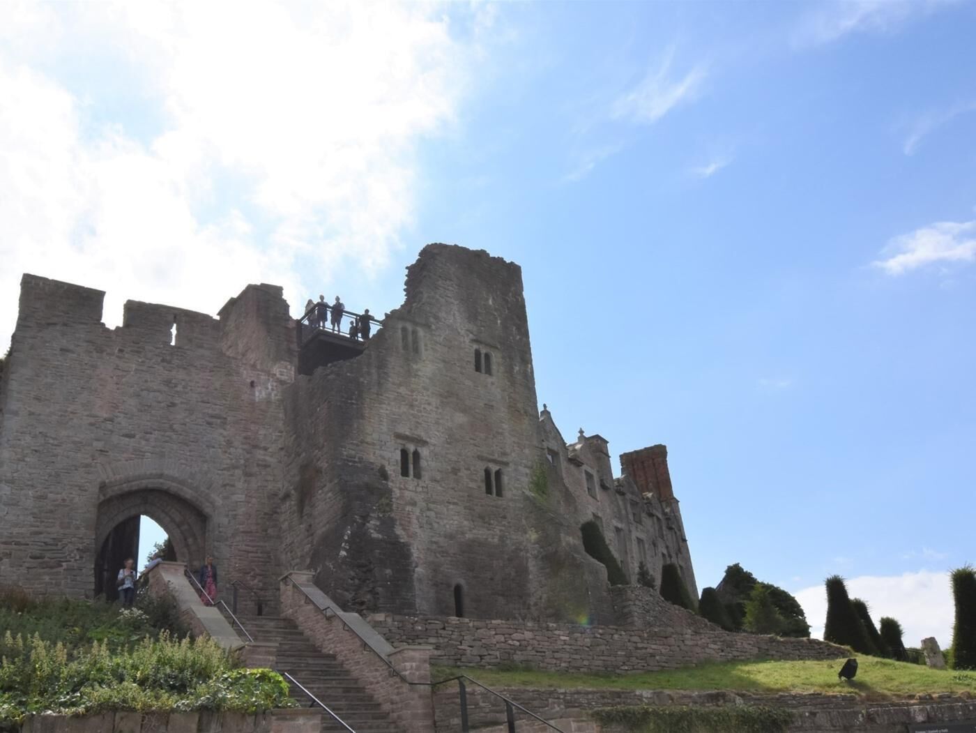 A historic stone castle with a large arched entrance, a staircase leading up to the main structure, and a clear sky above.