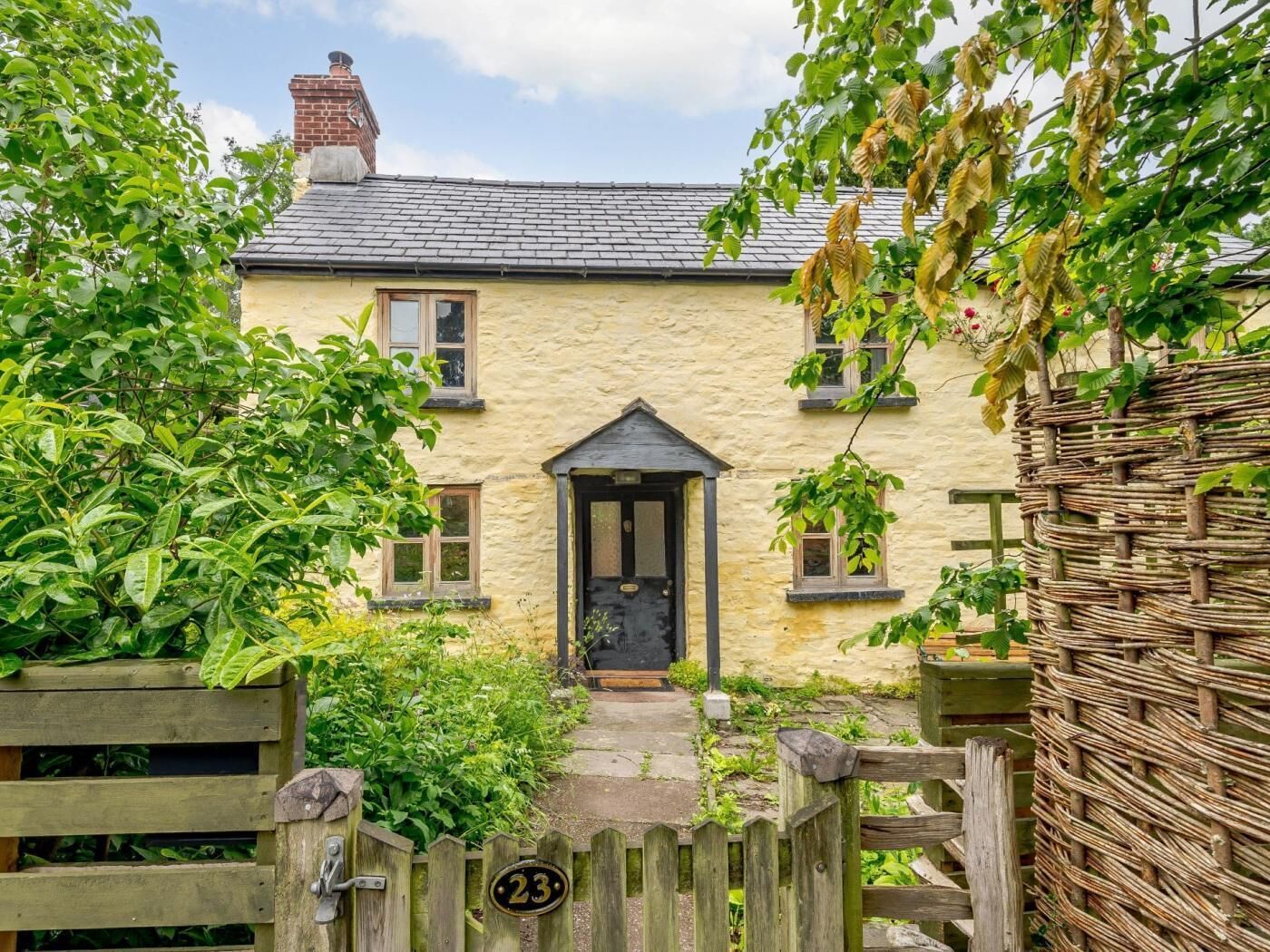 A quaint stone house with a wooden gate, a number 23 sign, and a traditional door.