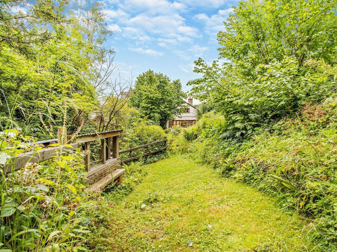 A pathway leading to a house surrounded by dense greenery and a wooden fence.