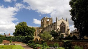 A historic building with a prominent clock tower, surrounded by well-maintained gardens and a paved walkway. - 2 Bed in Hexham (oc-88443) (Acomb)