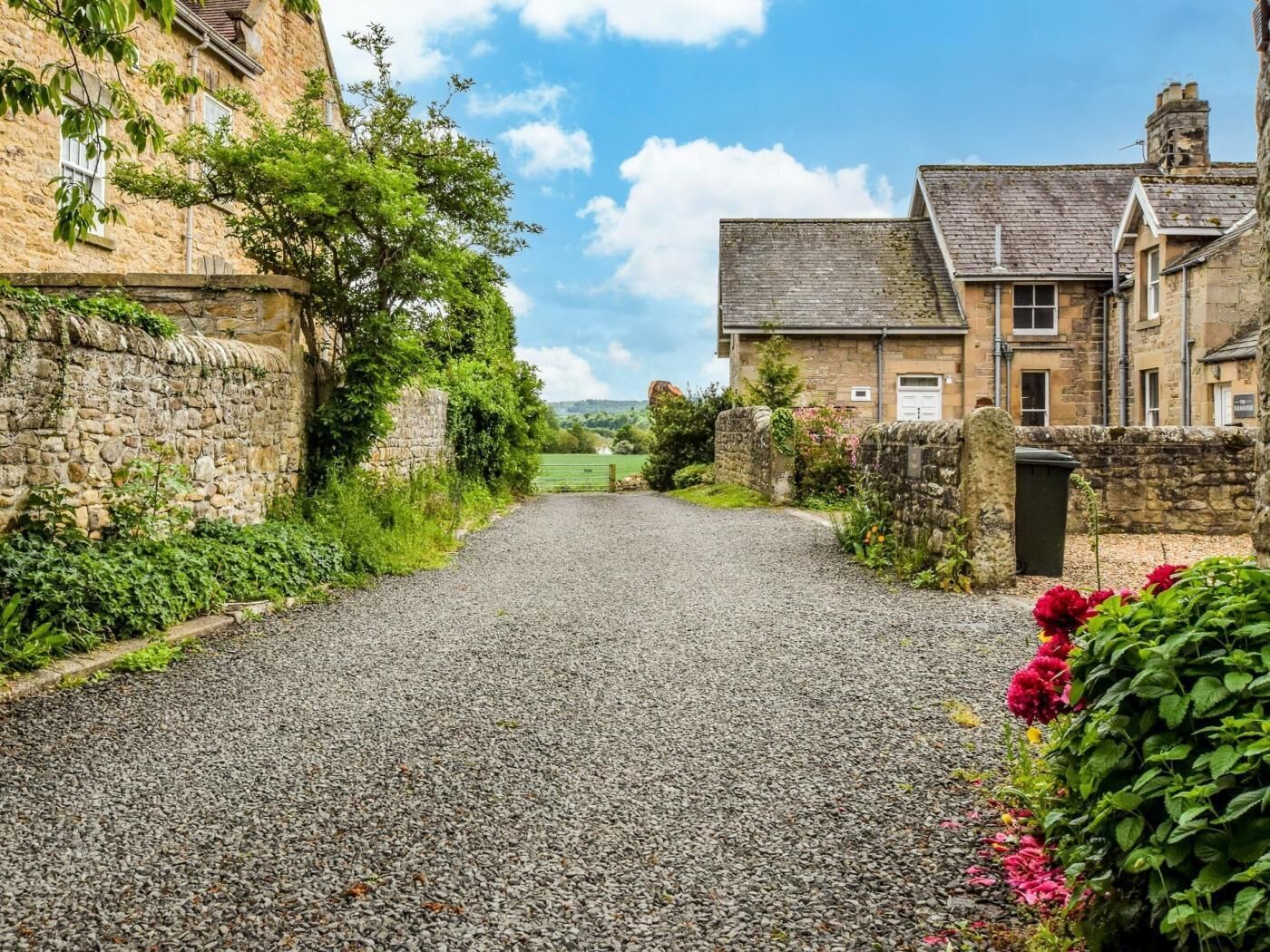 Un chemin de campagne mène à un bâtiment en pierre au style traditionnel, entouré de verdure et de murs de pierre.