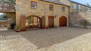 A stone building with a gravel driveway, wooden doors, and a small garden area. - 2 Bed in Hexham (oc-88443) (Acomb)