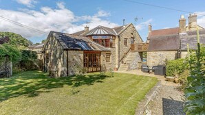 A stone house with a sloped roof, a wooden deck, and a grassy yard. - 2 Bed in Hexham (oc-88443) (Acomb)
