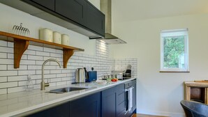 A modern kitchen with dark cabinets, a white countertop, and a window with a view of trees.