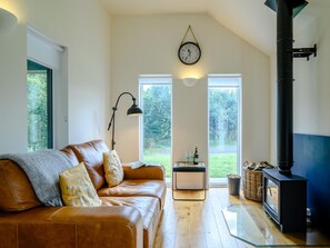 A cozy living room with a leather sofa, a glass coffee table, a fireplace, and a clock on the wall.