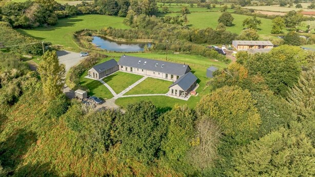 A large, rectangular building with a flat roof, surrounded by green fields and a small pond.
