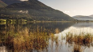 Een kalm meer met omliggende bergen en rietkragen op de voorgrond.