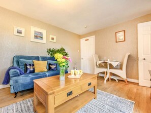 Ein Wohnzimmer mit einem blauen Sofa, einem Holztisch und einem Essbereich mit einem weißen Tisch und Stühlen.