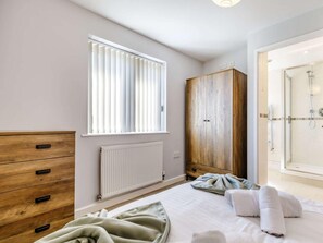 Un dormitorio con cama, armario de madera, radiador y ventana con persianas.