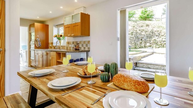 Cocina moderna con armarios de madera, una mesa de comedor para cuatro personas y un ventanal con vistas al exterior.