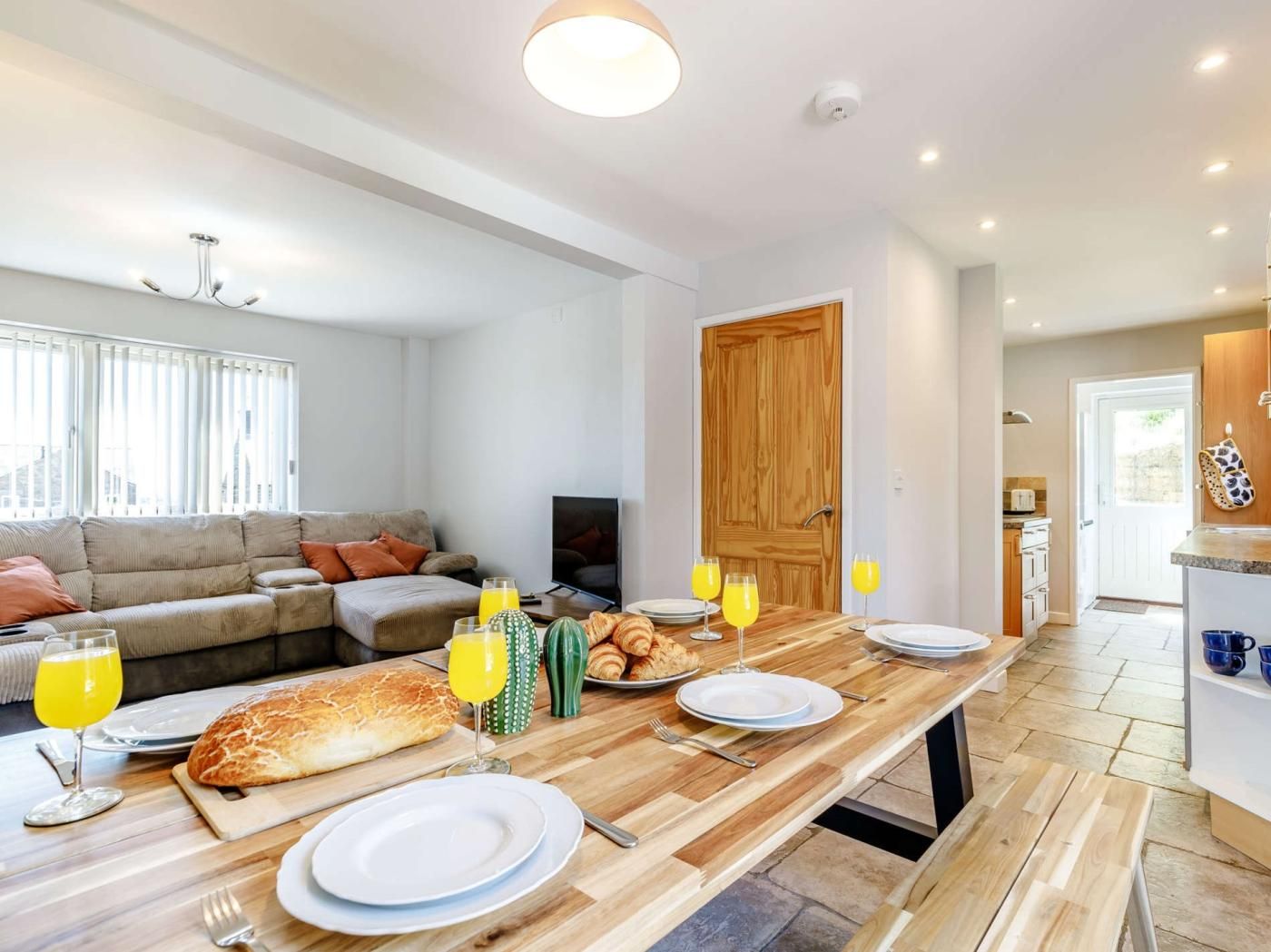 Un soggiorno moderno con un divano, un tavolo da pranzo apparecchiato per la colazione e una zona cucina visibile attraverso una porta aperta.