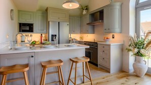 Una cocina moderna con una isla central, taburetes de bar, un ventanal grande y un florero decorativo.
