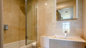 Un baño con cabina de ducha de vidrio, inodoro blanco y tocador con cajones.