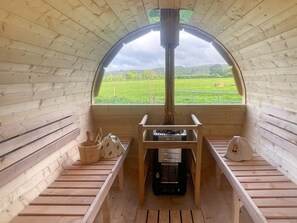 Eine Holzhütte mit einem zentralen Kamin, Holzbanken und Blick auf eine grüne Landschaft.