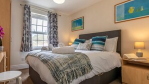 Un dormitorio con cama, mesitas de noche, una ventana con cortinas, un cuadro en la pared y una lámpara.