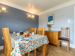 A dining area with a table set for four, wooden chairs, a patterned tablecloth, and a vase with flowers on the wall. - 3 Bed in Braunton (oc-87752) (Croyde)