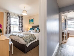 A bedroom with a bed, bedside table, and a window with curtains. - 3 Bed in Braunton (oc-87752) (Croyde)