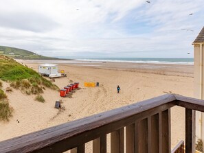 Ein Strand mit einer Holzterrasse, einem Rettungsschwimmerstand und einer Person, die am Sand entlanggeht.