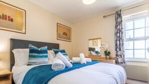 Una habitació d'hotel amb un llit, una taula de nit, un mirall, una finestra amb cortines i obra d'art a les parets.