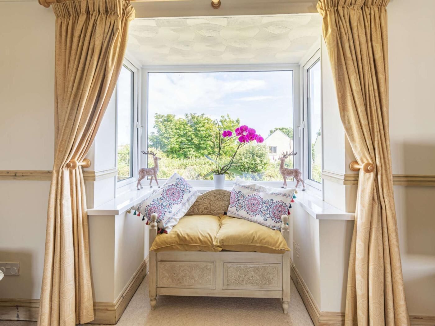 A room with a window seat, a bed with patterned pillows, and two deer figurines.