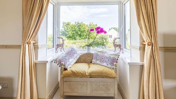 Una habitación con una ventana acolchada, una cama con almohadas estampadas y dos figuras de ciervo.