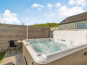 A hot tub in a backyard with a wooden fence, a chair, and a table with drinks. - 4 Bed in Haverfordwest (oc-88331) (Saint Ishmael's)