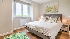 Um quarto com uma cama, janela, radiador, mesa de cabeceira e um quadro.