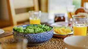 Ein Esstisch mit einer blauen, gemusterten Salatschüssel, einem Glas Orangensaft und einem Teller mit Obstscheiben.