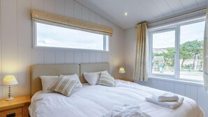 En pænt redt seng med puder, et natbord med en lampe og et vindue med gardiner.