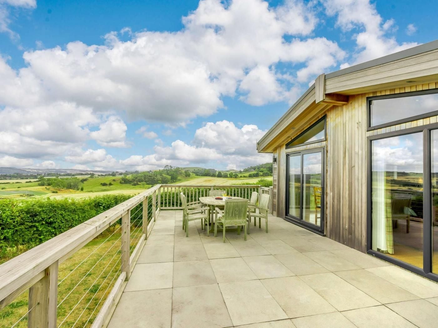 A balcony with a table and chairs, overlooking a green landscape.