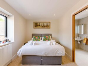 Ein Schlafzimmer mit einem Bett, einem Fenster, einem Heizkörper, einem Gemälde und einem Badezimmer mit Waschbecken und Spiegel.