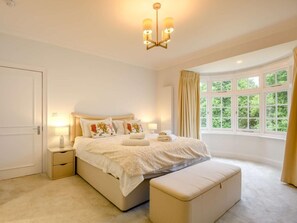 A bedroom with a large bed, bedside tables, a bench, a window with curtains, and a chandelier. - 7 Bed in King's Lynn (oc-88492) (Snettisham)
