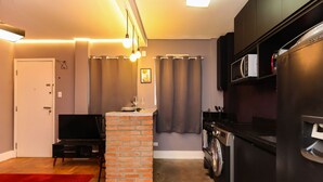 Un espacio habitable pequeño con chimenea de ladrillo, lavadora, refrigerador y televisor.