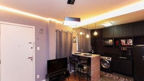 Un espacio habitable compacto con kitchenette, lavadora, televisión de pantalla plana y comedor con sillas.