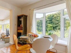 A dining area with a table set for two, a wooden cabinet, and a view of greenery outside. - 2 Bed in St. Austell (oc-88402) (Mevagissey)
