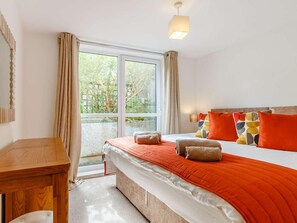 A bedroom with a bed, a bedside table, a lamp, and a view of greenery outside. - 2 Bed in St. Austell (oc-88402) (Mevagissey)