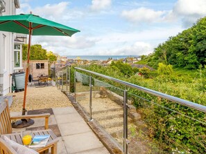 Een balkon met een metalen hekwerk, een groene parasol en een tafel met een stoel.