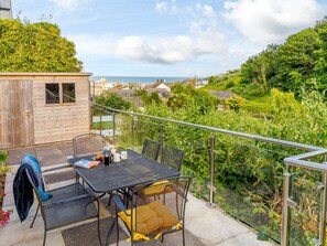 A patio with a table and chairs, overlooking a lush garden and a coastal view. - 2 Bed in St. Austell (oc-88402) (Mevagissey)