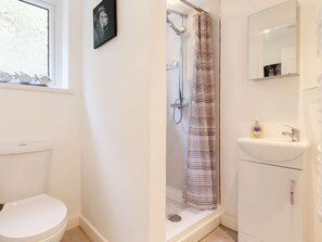 A bathroom with a toilet, a shower with a patterned curtain, a sink with a mirror, and a window with a picture. - 2 Bed in St. Austell (oc-88402) (Mevagissey)