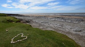A coastal landscape with a pebble beach, grassy areas, and a clear sky.