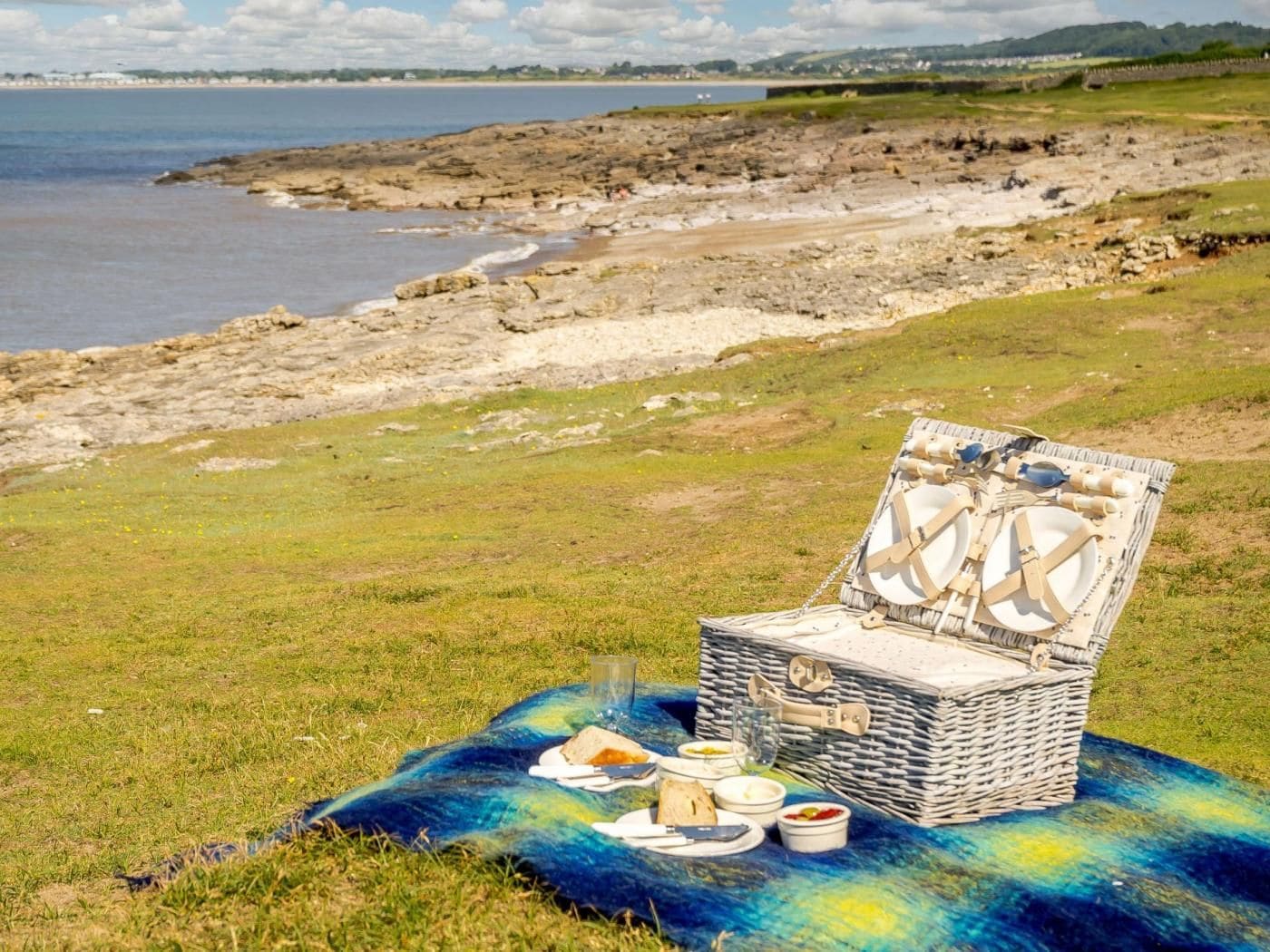 Ein Picknick mit einem Korbsessel und einer Decke auf einer Wiese in der Nähe einer felsigen Küste.