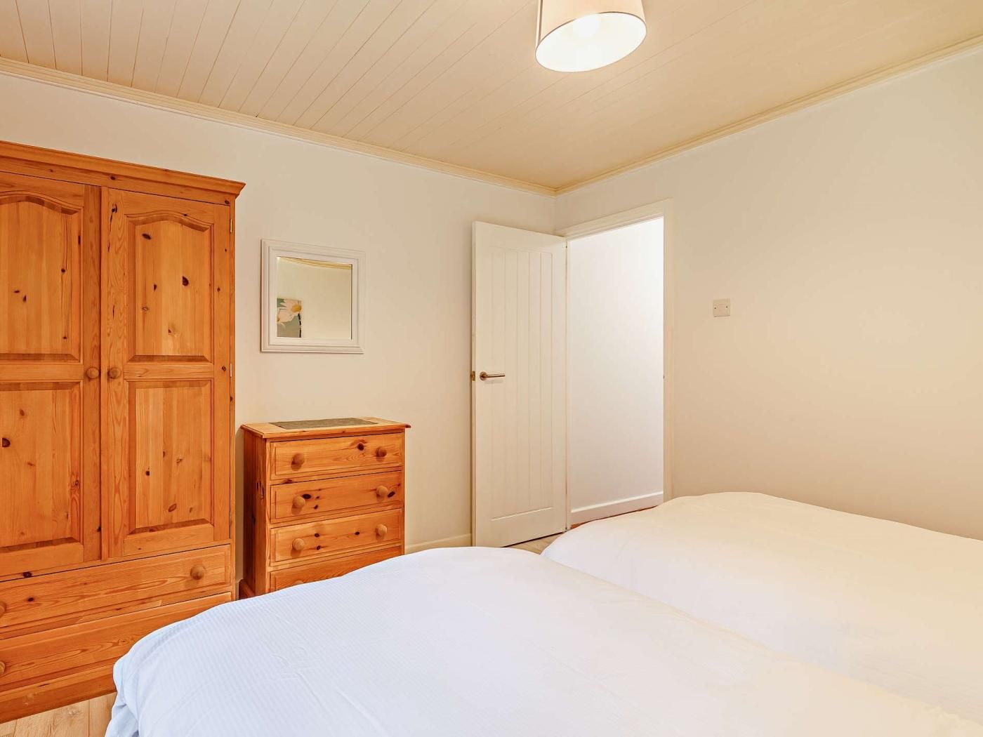 Quarto com duas camas, guarda-roupa de madeira, penteadeira e porta que dá para outro cômodo.