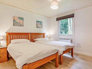 A bedroom with a wooden bed, two bedside tables, a nightstand, a window with a view of trees, and two wall-mounted flower paintings. - 2 Bed in Saltash (oc-88312) (Notter)