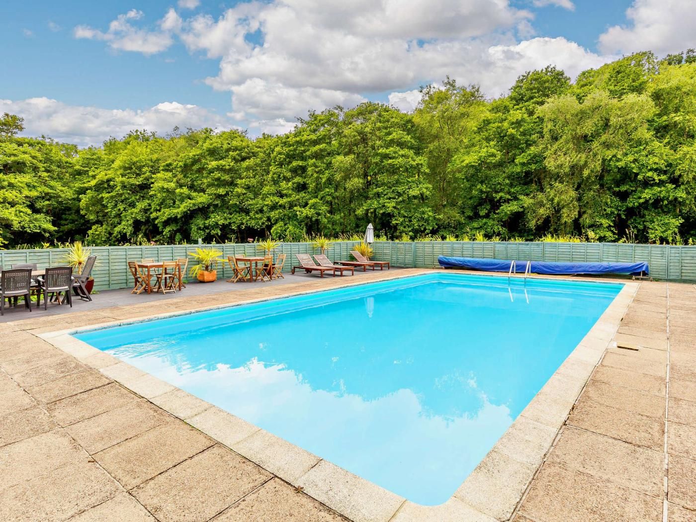 A rectangular swimming pool with a tiled edge, surrounded by a wooden deck.