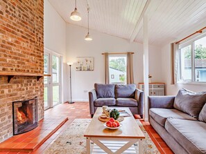 A living room with a brick fireplace, two sofas, a coffee table with fruit, and a painting on the wall. - 2 Bed in Saltash (oc-88312) (Notter)